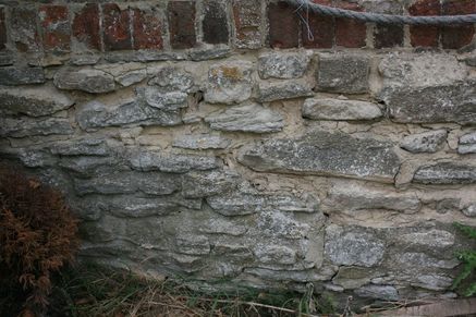 A stone wall of local limestone with red brick walling above.
